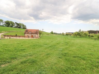 A small brick house with a red roof surrounded by a fenced green field and trees at Shepherd's Barn Between Milborne St Andrew and Winterborne Whitechurch