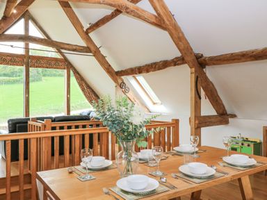 A dining table set with bowls glasses and cutlery near wooden beams and windows showing a green field at Shepherd's Barn Between Milborne St Andrew and Winterborne Whitechurch