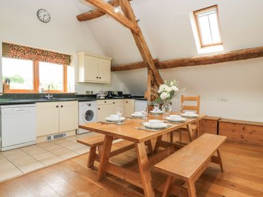 A kitchen and dining area with a wooden table set for six and exposed wooden beams at Shepherd's Barn Between Milborne St Andrew and Winterborne Whitechurch