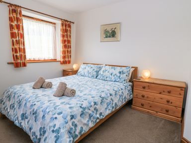 A bedroom with a double bed with blue patterned bedding two wooden dressers and a window with patterned curtains at Shepherd's Barn Between Milborne St Andrew and Winterborne Whitechurch