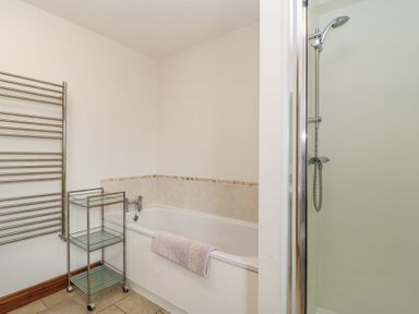 A bathroom with a bathtub towel rack glass shelving unit and a shower at Shepherd's Barn Between Milborne St Andrew and Winterborne Whitechurch