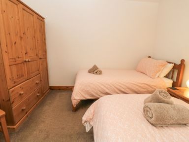 A bedroom with two single beds with pink bedding and towels on each bed and a wooden wardrobe at Shepherd's Barn Between Milborne St Andrew and Winterborne Whitechurch