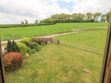 A garden with bushes and a lawn next to a wooden fence and green fields at Shepherds Barn Between Milborne St Andrew and Winterborne Whitechurch