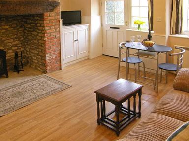 A room with a stone and brick fireplace a small black table a dining table with two chairs and a sofa at Candy Cottage Thornford near Sherborne