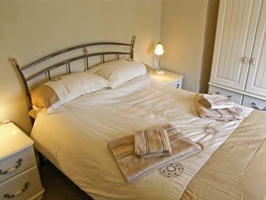 A bedroom with a double bed with towels on it two bedside tables with lamps and a white wardrobe at Candy Cottage in Thornford near Sherborne