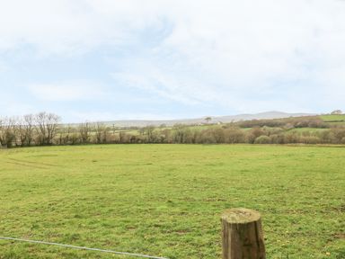 A large green field with a wooden post in the foreground and trees and hills in the background at Saddlers Cottage Berllandeg Farm Clunderwen near Narberth