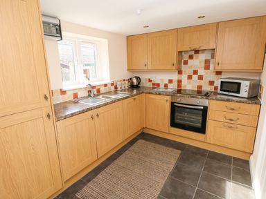 A kitchen with wooden cabinets a built in oven a microwave and a window at Saddlers Cottage Berllandeg Farm Clunderwen near Narberth
