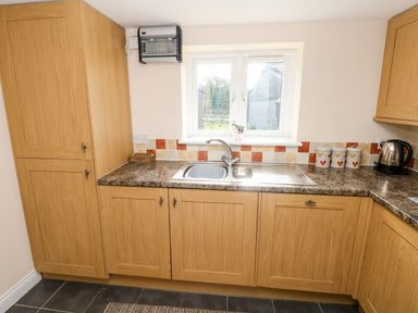 A kitchen with wooden cabinets a double sink a tiled backsplash and a window at Saddlers Cottage Berllandeg Farm in Clunderwen near Narberth