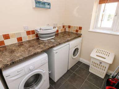 A utility room with a washing machine, a fridge, a laundry basket, and a countertop at Saddlers Cottage Berllandeg Farm Clunderwen near Narberth