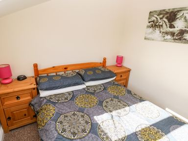 A bedroom with a wooden double bed with patterned bedding and matching wooden bedside tables with pink lamps and a horse picture on the wall at Saddlers Cottage Berllandeg Farm Clunderwen near Narberth