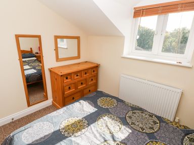 A bedroom with a bed covered in patterned bedding a wooden dresser and two mirrors on the wall at Saddlers Cottage Berllandeg Farm Clunderwen near Narberth
