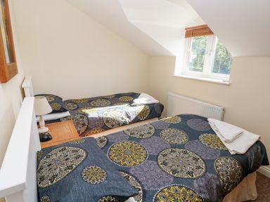 A bedroom with two single beds with patterned bedspreads a bedside table and a window at Saddlers Cottage Berllandeg Farm in Clunderwen near Narberth