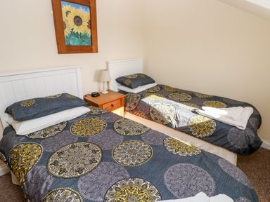 A bedroom with two single beds pillows patterned bedspreads a wooden nightstand lamp and framed sunflower painting at Saddlers Cottage Berllandeg Farm Clunderwen near Narberth