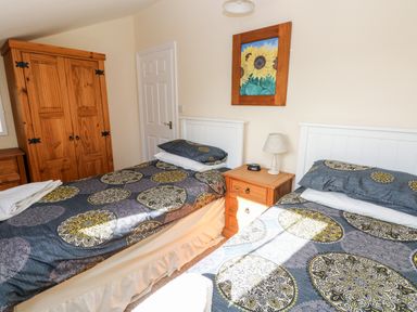 A bedroom with two single beds a wooden wardrobe and a nightstand with lamp and clock at Saddlers Cottage Berllandeg Farm Clunderwen near Narberth