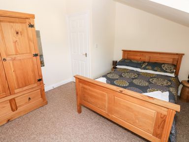 A bedroom with a wooden bed and wardrobe a door and carpeted floor at Saddlers Cottage Berllandeg Farm in Clunderwen near Narberth