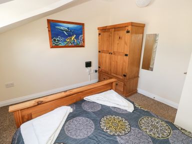 A bedroom with a wooden bed and wardrobe a framed painting on the wall and a mirror on the right wall at Saddlers Cottage Berllandeg Farm in Clunderwen near Narberth