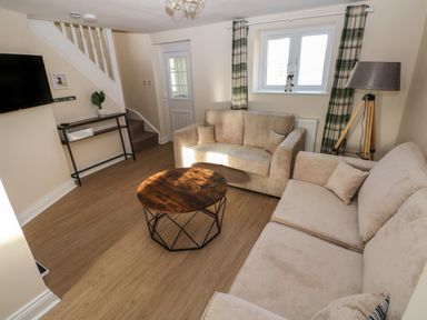 A living room with two beige sofas a round wooden coffee table a TV mounted on the wall stairs a floor lamp and a window with plaid curtains at Saddlers Cottage Berllandeg Farm Clunderwen near Narberth