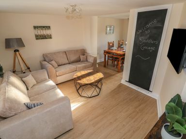 A living room with two beige sofas a wooden coffee table a tripod lamp and a dining table at Saddlers Cottage Berllandeg Farm