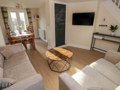 A living room with two beige sofas and a round wooden coffee table next to a dining table set with plates and glasses at Saddlers Cottage Berllandeg Farm in Clunderwen near Narberth