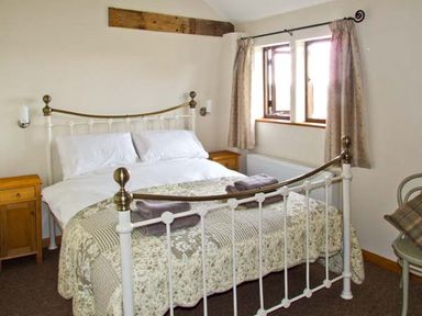 A bedroom with a metal bed frame two bedside tables and a window with curtains at Bushmills in Kerrys Gate near Abbey Dore