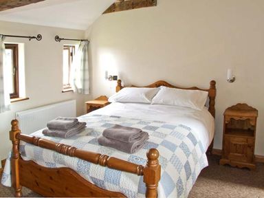 A bedroom with a wooden bed with white and blue plaid bedding and folded towels on it at Bushmills Kerry's Gate near Abbey Dore