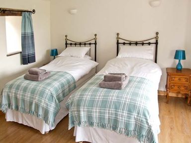 A bedroom with two single beds each with blue plaid blankets and towels on top at Bushmills Kerry's Gate near Abbey Dore