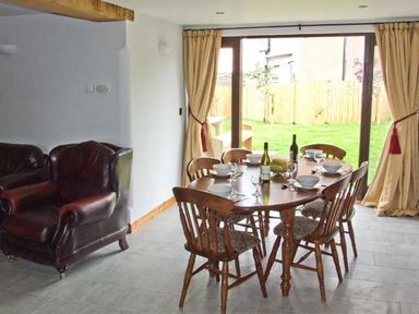 A dining area with a wooden table set for six and leather armchairs near sliding glass doors at Bushmills in Kerry's Gate near Abbey Dore