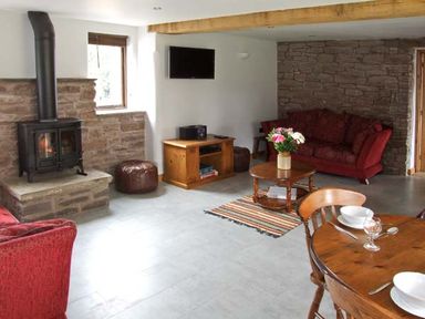 A living room with a wood-burning stove red sofas wooden coffee table with flowers and a dining table at Bushmills in Kerrys Gate near Abbey Dore