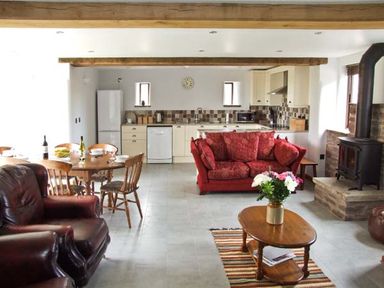 An open plan kitchen and living area with wooden dining table and chairs red sofa and wood stove at Bushmills in Kerrys Gate near Abbey Dore