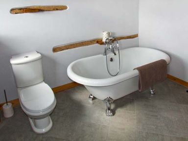 A bathroom with a toilet a clawfoot bathtub with a towel and a mug on the wooden shelf on the wall