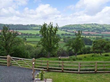 A fenced yard with trees and grassy fields in the background at Bushmills Kerry's Gate near Abbey Dore