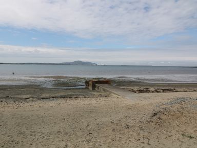 A sandy beach with a concrete ramp extending into the water and hills in the background at Ty Fferm Bodlasan in Llanfachraeth near Valley
