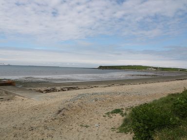 A beach with sand sea and grassy area at Ty Fferm Bodlasan in Llanfachraeth near Valley
