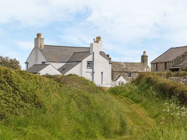 A path between grass and bushes leads to white and stone houses with chimneys at Ty Fferm Bodlasan in Llanfachraeth near Valley