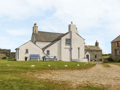A white house with blue trim and a blue bench and picnic table on a grassy area at Ty Fferm Bodlasan in Llanfachraeth near Valley