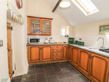 A kitchen with wooden cabinets a microwave kettle toaster and containers on the countertop at Ty Fferm Bodlasan in Llanfachraeth near Valley