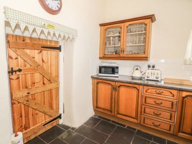 A kitchen with wooden cabinets a microwave kettle toaster and a wooden door with a caution sign at Ty Fferm Bodlasan in Llanfachraeth near Valley