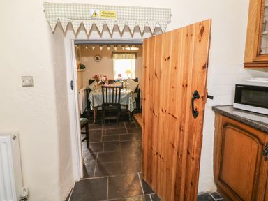 A wooden door opening to a dining area with a table and chairs covered with checkered cloth at Ty Fferm Bodlasan in Llanfachraeth near Valley