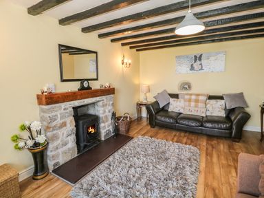 A living room with a stone fireplace black stove black leather sofa with pillows shaggy rug and wooden beams on ceiling at Ty Fferm Bodlasan Llanfachraeth near Valley