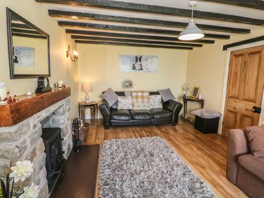 A living room with a leather sofa wooden floor stone fireplace and a shaggy rug at Ty Fferm Bodlasan Llanfachraeth near Valley