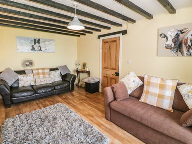 A living room with two sofas a wooden door wooden beams on the ceiling and animal paintings at Ty Fferm Bodlasan in Llanfachraeth near Valley