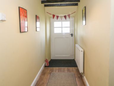 A narrow hallway with yellow walls wooden floor a white door with window panels and heart decorations at Ty Fferm Bodlasan Llanfachraeth near Valley