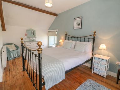 A bedroom with a metal bed frame bedside tables with lamps a dresser and a chair at Ty Fferm Bodlasan in Llanfachraeth near Valley
