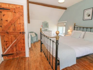 A bedroom with a metal bed frame wooden door wooden floor and a chair at Ty Fferm Bodlasan in Llanfachraeth near Valley