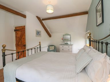 A bedroom with a metal bed frame dresser chair wooden door and exposed ceiling beams at Ty Fferm Bodlasan Llanfachraeth near Valley