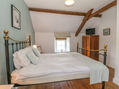 A bedroom with a metal bed, wooden floor, small window, and wooden cabinet with a television at Ty Fferm Bodlasan Llanfachraeth near Valley