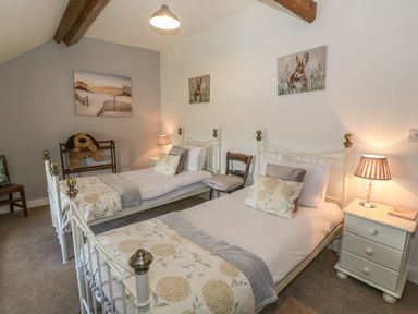 A bedroom with two single beds bedside tables with lamps and wall art at Ty Fferm Bodlasan in Llanfachraeth near Valley