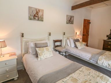 A bedroom with two single beds a wooden chair bedside tables with lamps and rabbit paintings on the wall at Ty Fferm Bodlasan Llanfachraeth near Valley