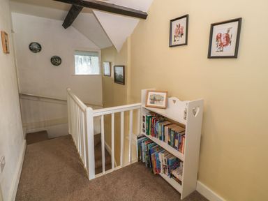 A hallway with a small white bookshelf filled with books and framed pictures on the walls at Ty Fferm Bodlasan in Llanfachraeth near Valley