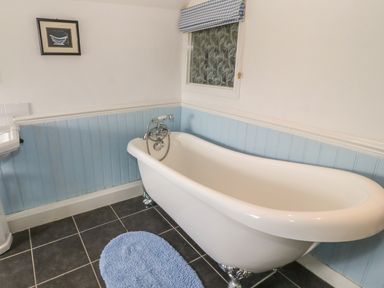 A bathroom with a white clawfoot bathtub blue paneling and a blue rug on the floor at Ty Fferm Bodlasan Llanfachraeth near Valley